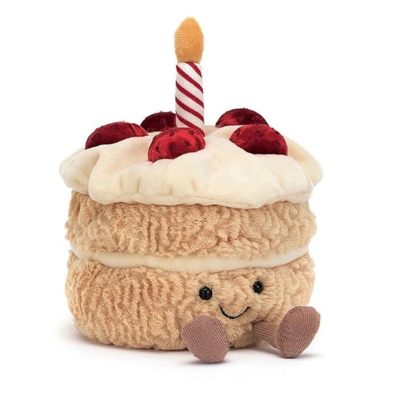 Jellycat Amuseables Birthday Cake front view — golden sponge plush cake with cream filling layer, white icing top, red cherry decorations, red and white striped candle and brown corduroy feet with embroidered smiling face