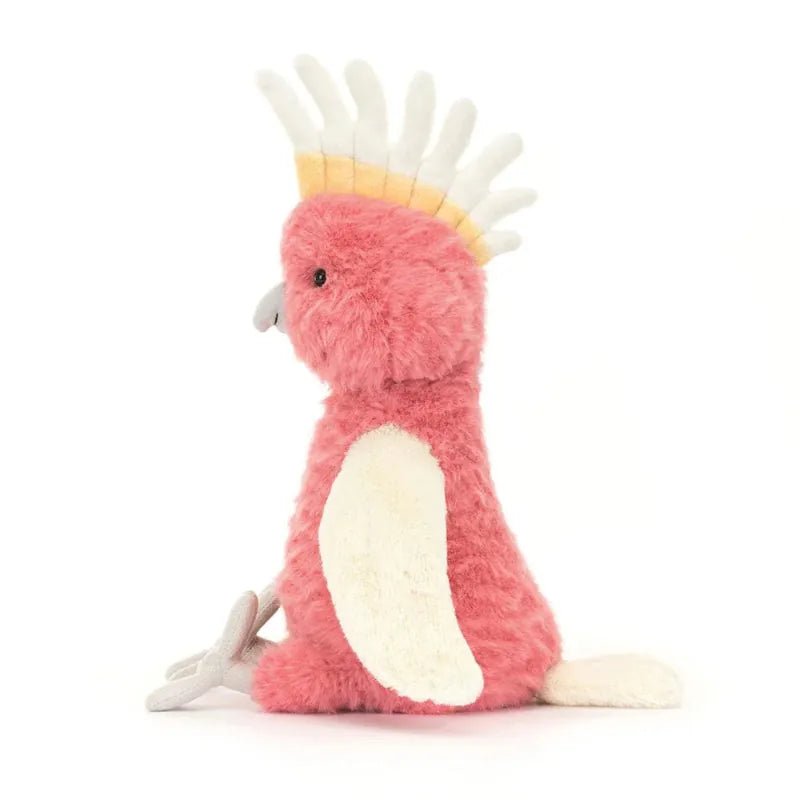 Jellycat Squawkatoo side view — coral pink plush cockatoo with white and yellow crest, grey beak, cream folded wing and grey tail feather