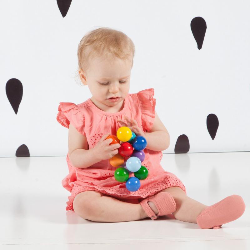 Baby girl in a pink outfit sitting on the floor and playing with a colourful bead grasping toy